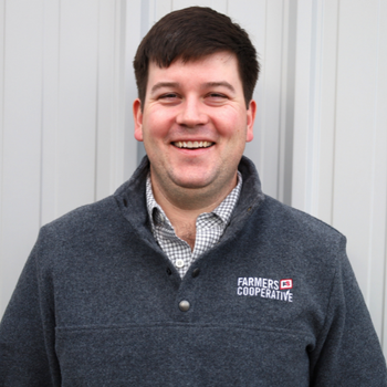 Man wearing a dark gray sweater with 'Farmers Cooperative' logo against a light background
