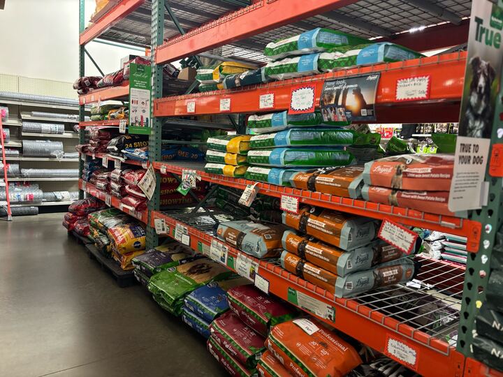 Shelves filled with colorful bags of pet food in a store aisle. Labels and price tags are visible, creating a busy and organized retail atmosphere.